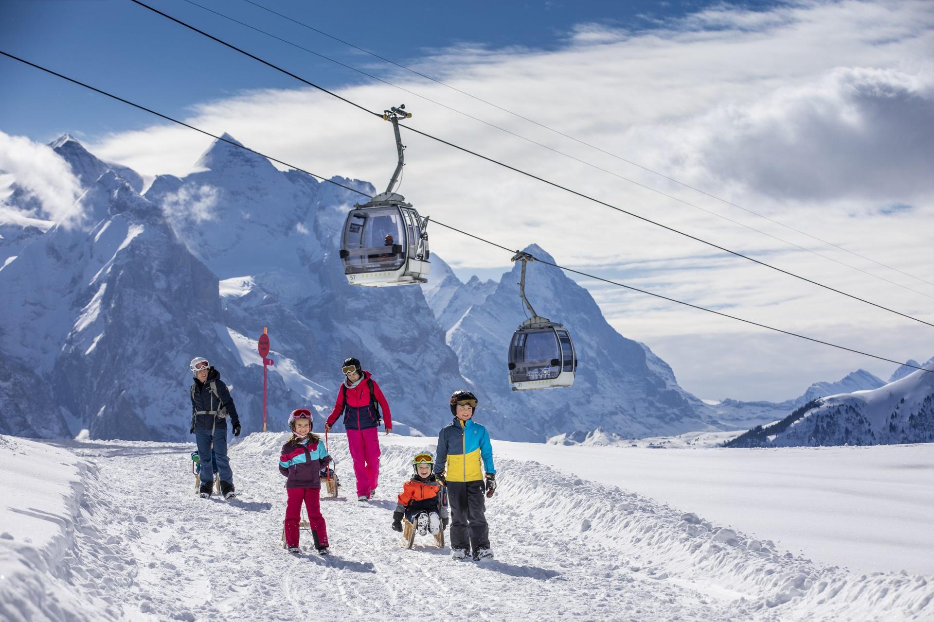Family walking under a gondola pulling sleds in Switzerland