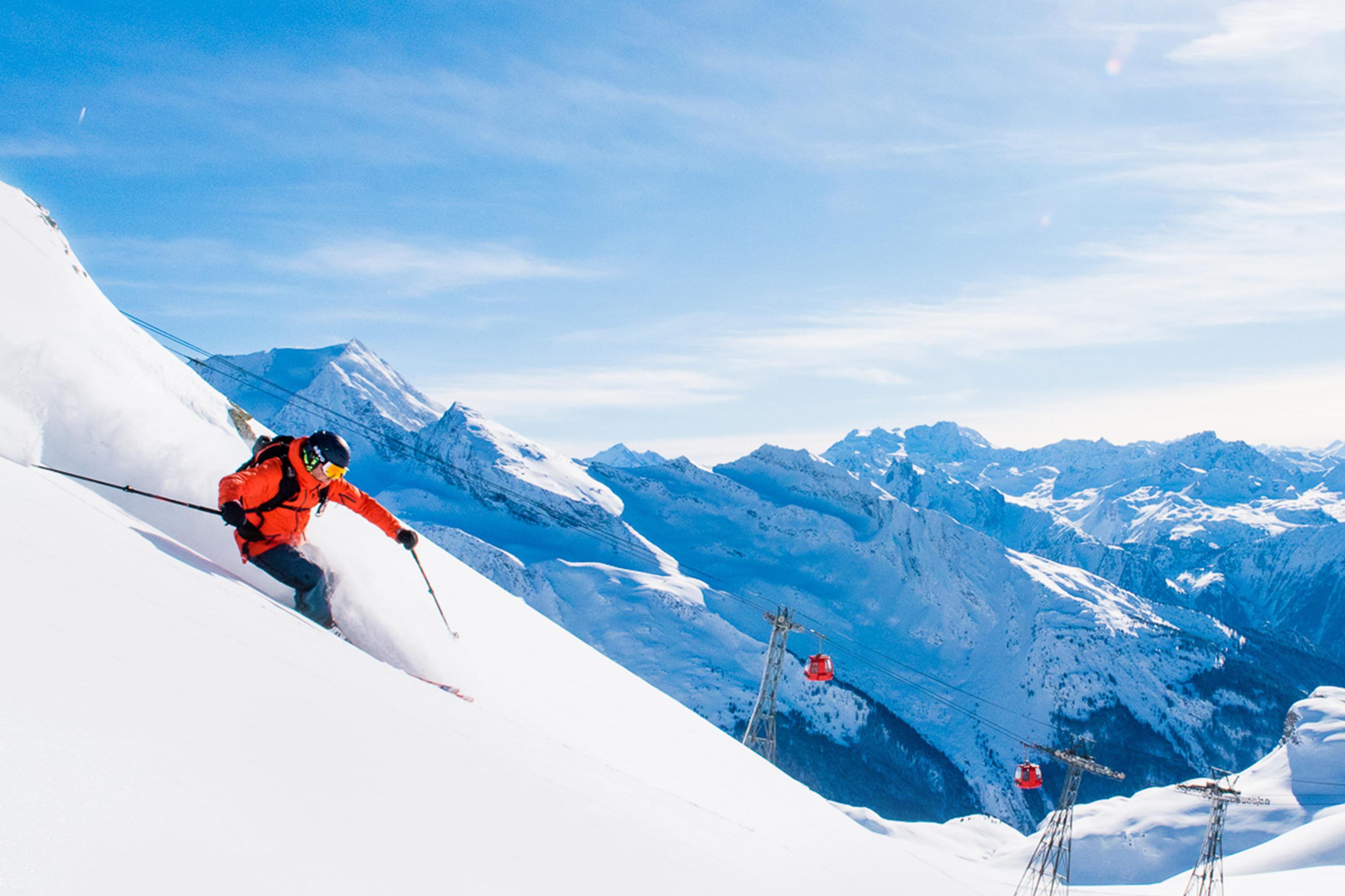 Skiier skiing down off-piste slope on sunny day