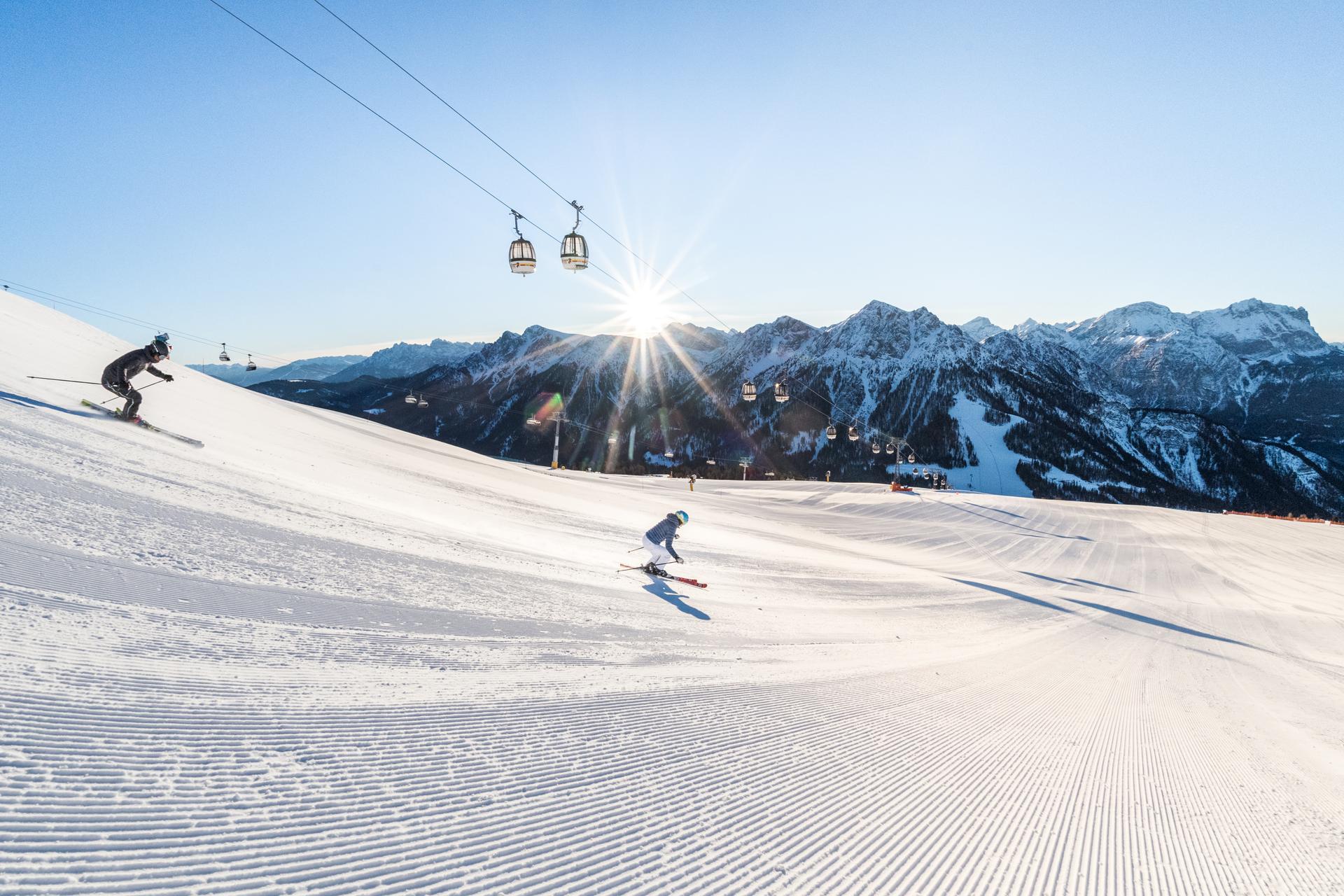 Skiiers skiing down wide open ski slope on sunny day